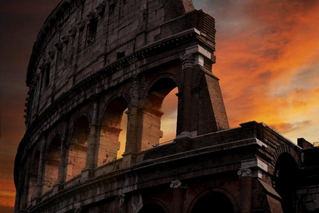 El emblemático Coliseo de Roma bañado por el cálido resplandor del sol poniente, creando una impresionante silueta contra el cielo.